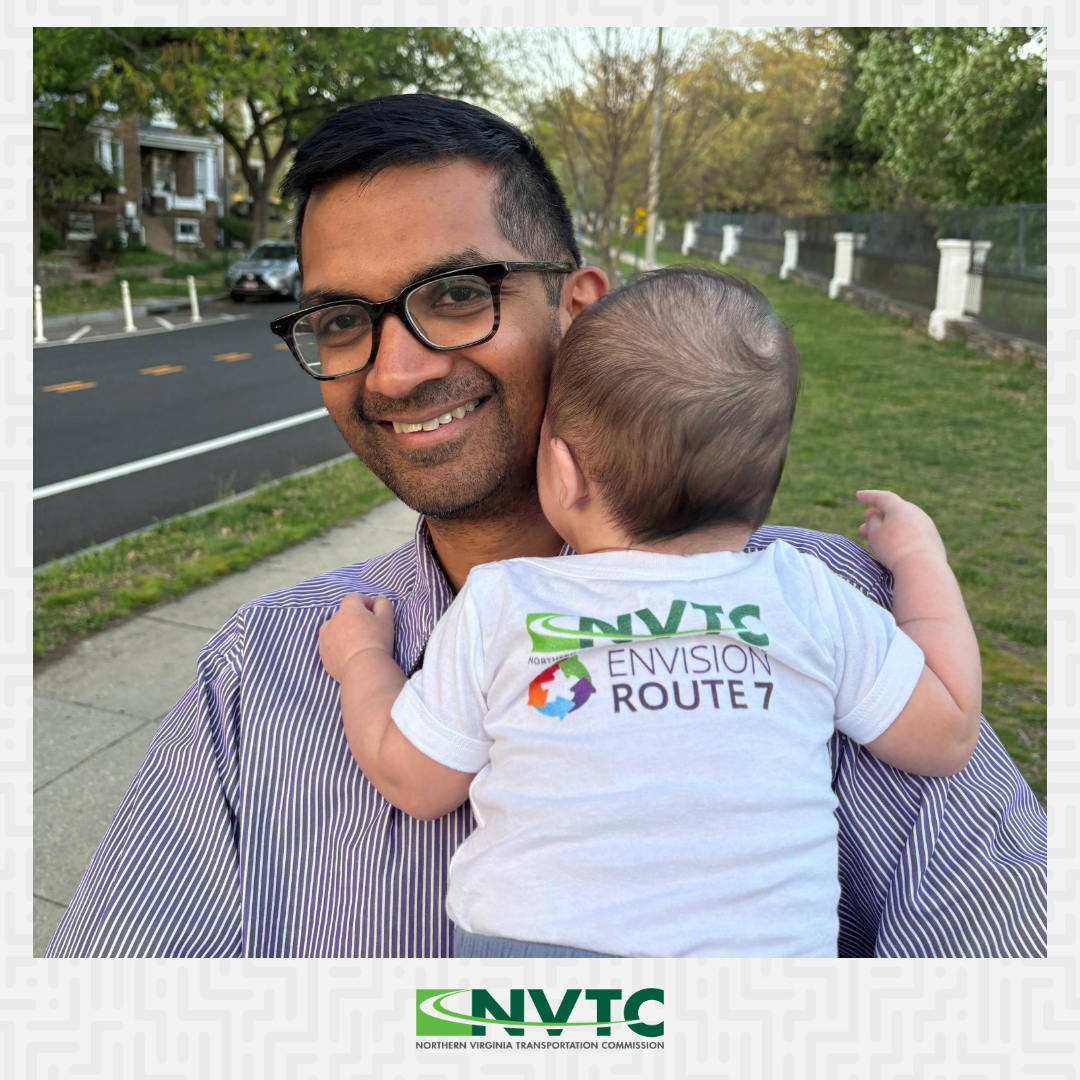 A photo of Envision Route 7's Vikram Sinha holding his new baby, whose back is to the camera so he can show off his Envision Route 7 onesie